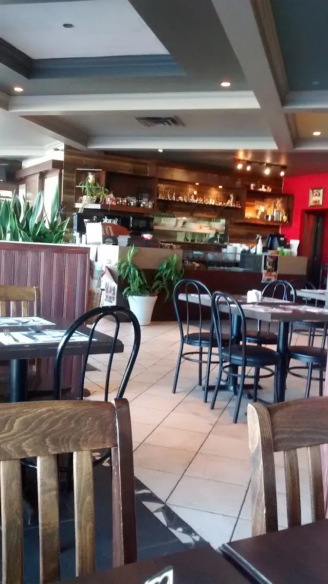 La salle du restaurant : tables de bistro, plantes vertes et, au fond, le comptoir café et ses tablettes de boutique.